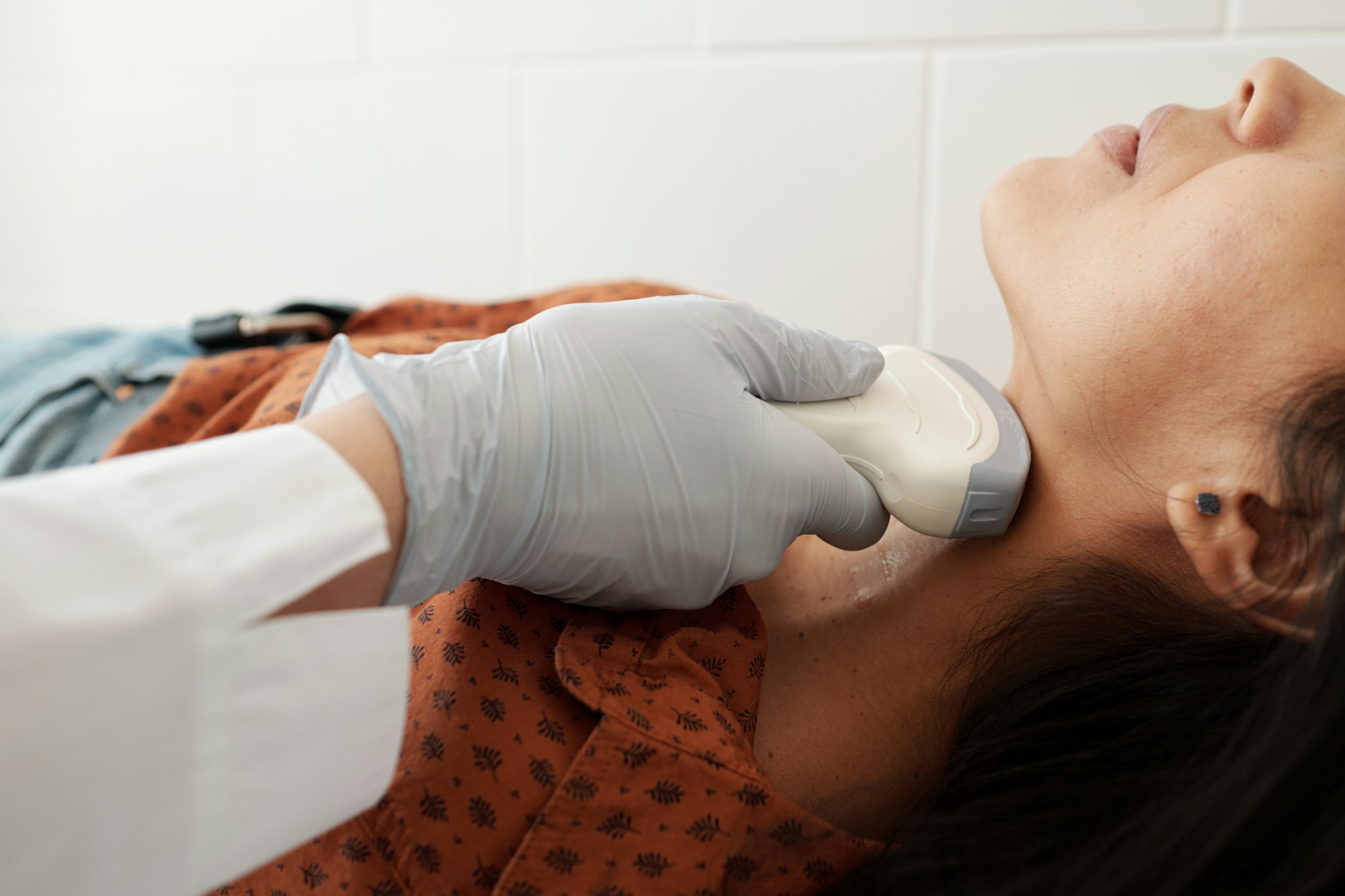 Gloved hand of doctor holding ultrasound scan on neck of patient