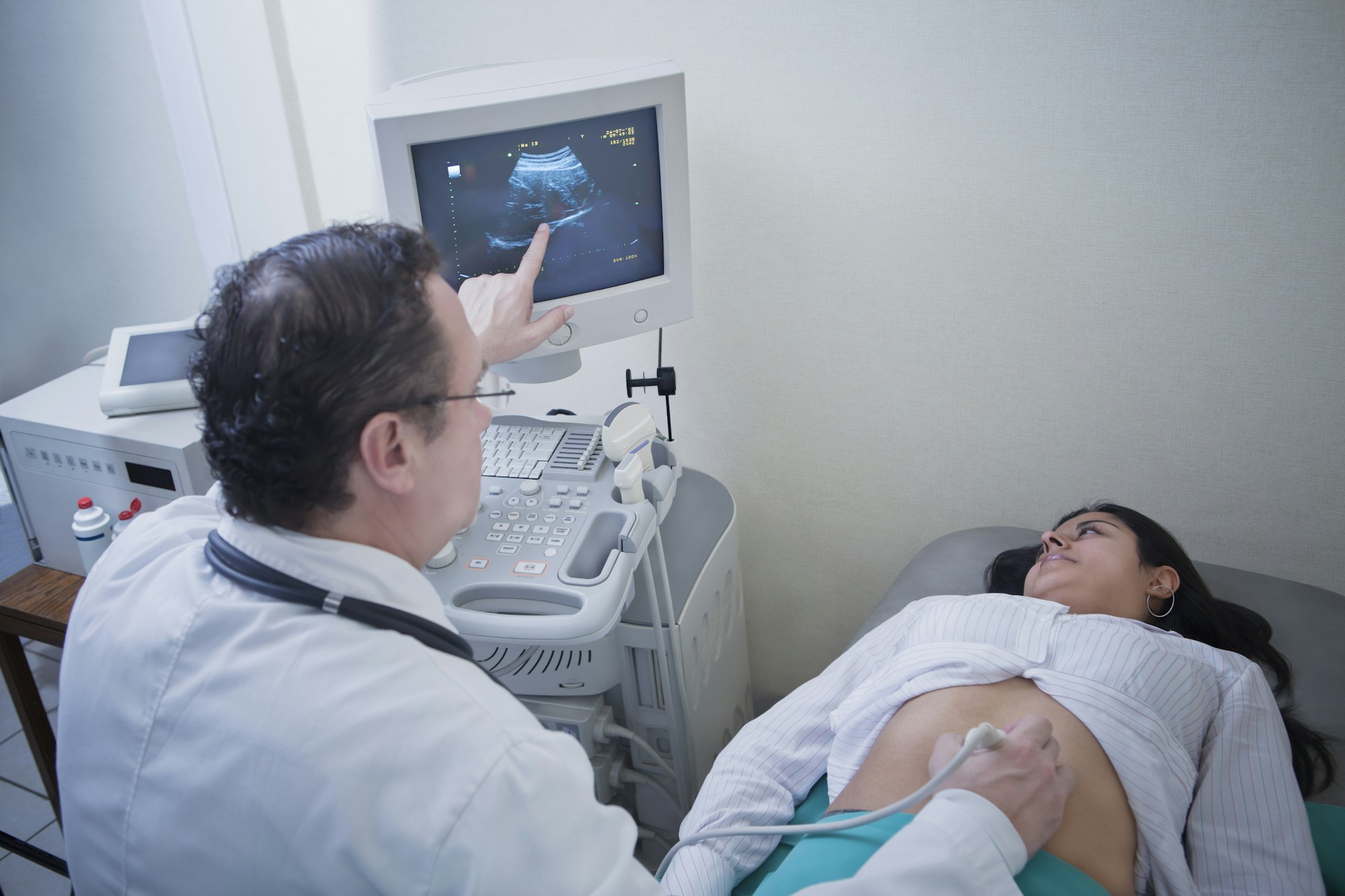 Sonographer and young woman looking at ultrasound scan on computer screen